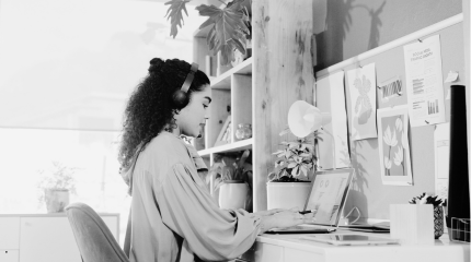 Woman wearing headphones and working at her laptop in a home office. 