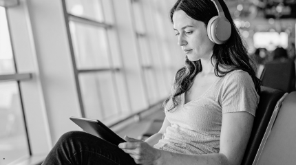 Woman uses her tablet while wiating for her flight to board - black and grey colouring 