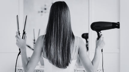 Woman styling her long hair, using a hair dryer and hair straighteners